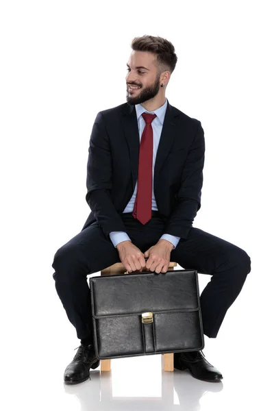 Jovem Empresário Feliz Segurando Mala Sorrindo Sentado Isolado Fundo Branco — Fotografia de Stock