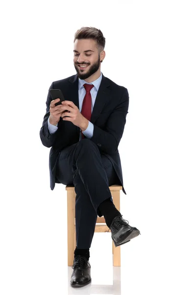 Улыбающийся Молодой Бизнесмен Смотрящий Телефон Сидящий Изолированный Белом Фоне — стоковое фото