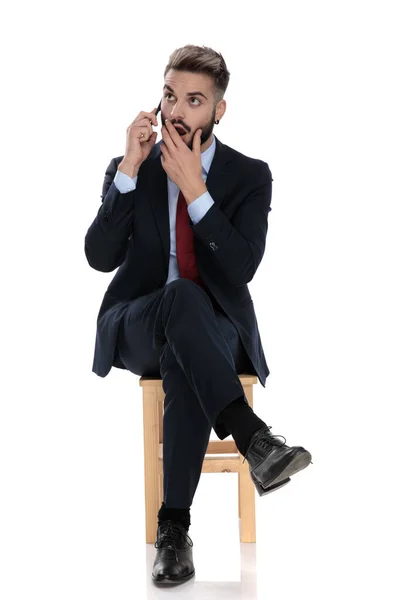 Chocado Jovem Empresário Falando Telefone Cobrindo Boca Com Mão Sentado — Fotografia de Stock