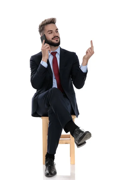 Jovem Empresário Falando Telefone Mostrando Dedo Médio Para Lado Sentado — Fotografia de Stock