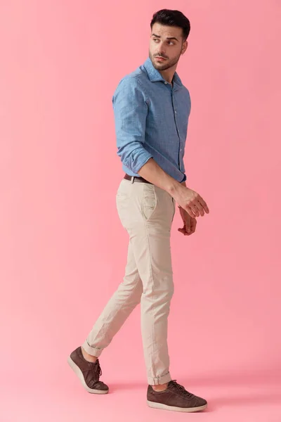 ピンク色のスタジオをバックに肩越しに歩きながら青いシャツを着た魅力的なビジネスマンの横顔 — ストック写真