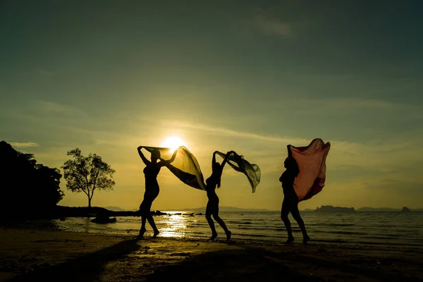 Silhouet van drie meisjes op het strand bij zonsondergang — Stockfoto