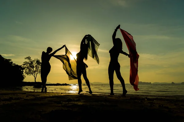 Silhouet van drie meisjes op het strand bij zonsondergang — Stockfoto