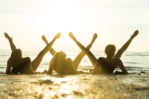 Silhueta de três meninas na praia ao pôr do sol — Fotografia de Stock