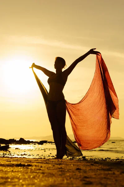 Silhouette di una donna giovane e in forma sulla spiaggia al tramonto — Foto Stock