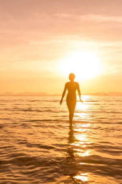 Gün batımında sahilde genç ve zinde bir kadının silueti.