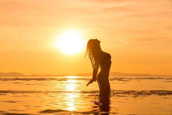 Silhouet van een jonge en fitte vrouw op het strand bij zonsondergang — Stockfoto