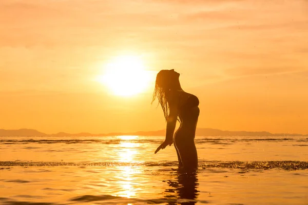 Silhueta de uma mulher jovem e apta na praia ao pôr do sol — Fotografia de Stock