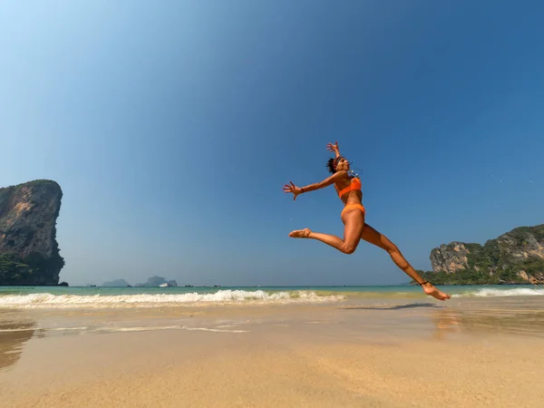 Zorgeloos vrouw in bikini op het strand met armen outstret springen — Stockfoto
