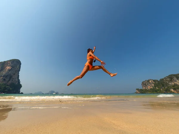 Unbekümmerte Frau im Bikini springt mit ausgestreckten Armen am Strand — Stockfoto