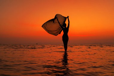 Gün batımında sahilde genç ve zinde bir kadının silueti.