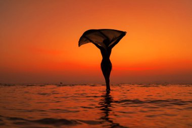 Gün batımında sahilde genç ve zinde bir kadının silueti.