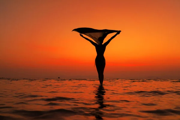 Silhueta de uma mulher jovem e apta na praia ao pôr do sol — Fotografia de Stock