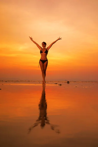 Silhouet van een jonge en fitte vrouw op het strand bij zonsondergang — Stockfoto