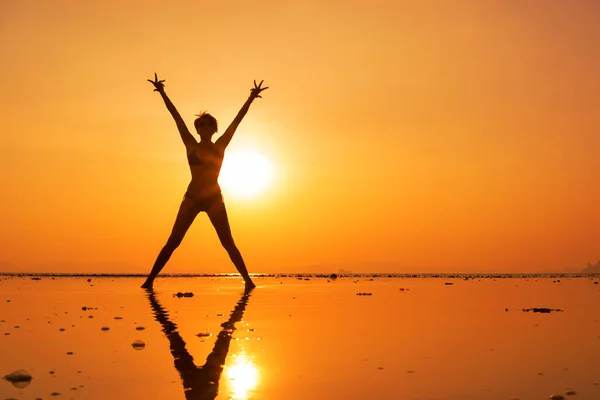 Silueta de una mujer joven y en forma en la playa al atardecer — Foto de Stock