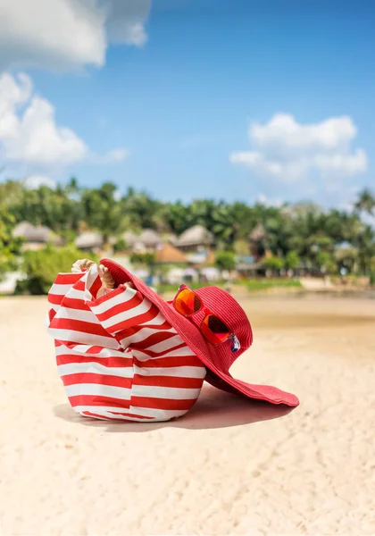 Соломенная шляпа, сумка, солнцезащитные очки и шлепанцы на тропическом пляже — стоковое фото