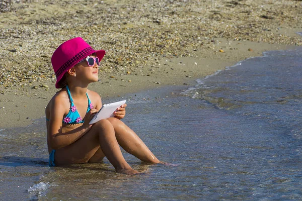 Маленька дівчинка з планшетом на пляжі під час літніх канікул — стокове фото