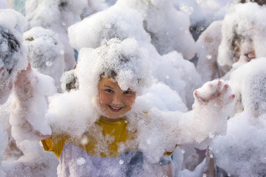 Foam Party on the beach. Cute little boy having fun and dancing.