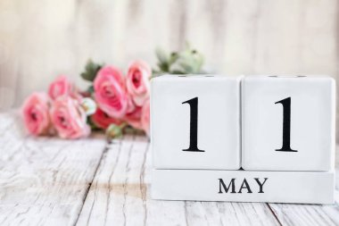 Ulusal Kadın Muayenesi için tarihi 11 Mayıs olan beyaz tahta takvim blokları. Arkaplanda pembe ranunculus olan seçici odak tahta bir masanın üzerinde.