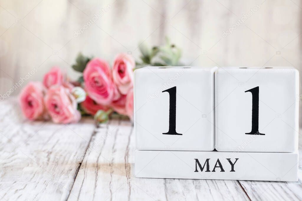 White wood calendar blocks with the date May 11 th for National Women's Checkup Day. Selective focus with pink ranunculus in the background over a wooden table.