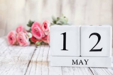 Uluslararası Hemşireler Günü için tarihi 12 Mayıs olan beyaz tahta takvim blokları. Arkaplanda pembe ranunculus olan seçici odak tahta bir masanın üzerinde.
