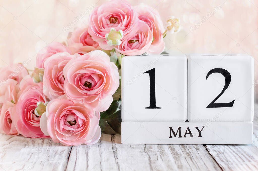 White wood calendar blocks with the date May 12th and pink ranunculus flowers over a wooden table for International Nurses Day.. Selective focus with blurred background. 