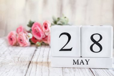 Uluslararası Anma Günü için 28 Mayıs tarihli beyaz tahta takvim blokları. Arkaplanda pembe ranunculus olan seçici odak tahta bir masanın üzerinde.