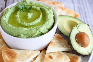 Vejetaryen avokado humusu, nohut, avokado ve tahini, zeytinyağı ile yapılır. Maydanozla süslenmiş ve kırsal bir masada pide ekmeğiyle servis edilmiş. Arkaplanı olan son derece sığ alan derinliği.