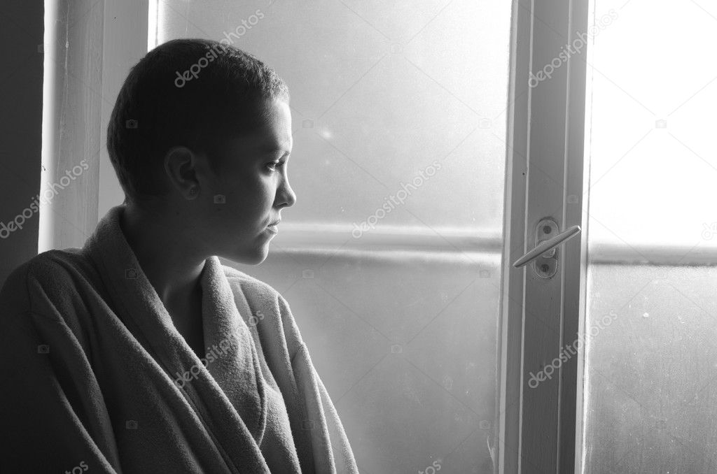 Young depressed cancer patient standing in front of hospital window