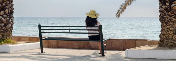 Giovane signora seduta sulla panchina e guardando il mare nella soleggiata giornata estiva — Foto Stock