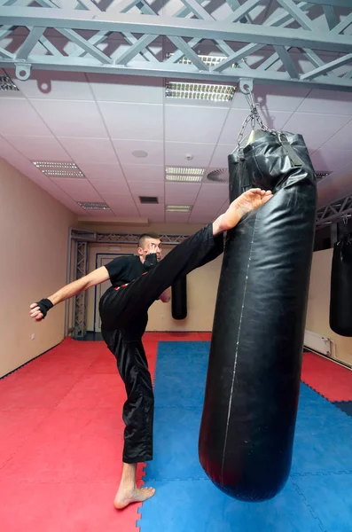 Young kickboxer kicking punching bag in sport gym — Stock Photo, Image