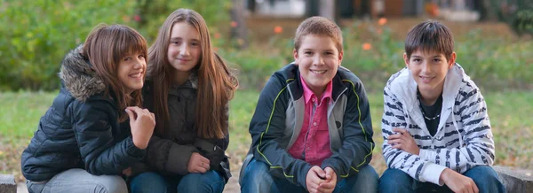 Szczęśliwy nastoletnich chłopców i dziewcząt, spoczywającej na ławce w parku w piękny jesienny dzień — Zdjęcie stockowe