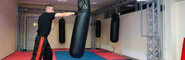 Joven kickboxer pateando y perforando saco de boxeo en gimnasio deportivo —  Fotos de Stock