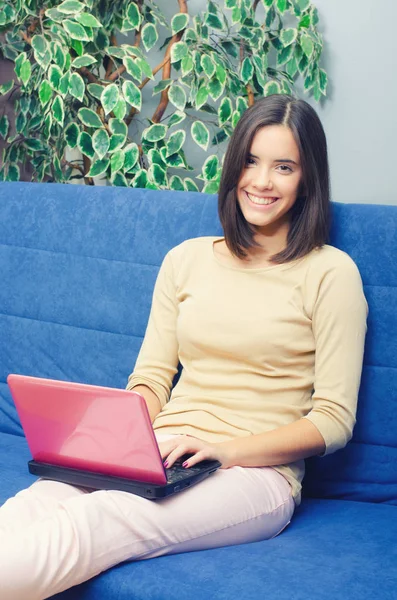 Young smiling girl using notebook while sitting on couch at home — Stock Photo, Image