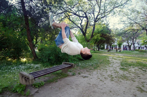 Teenage fitness parkour chlapec dělat salto dozadu od lavičky v parku — Stock fotografie