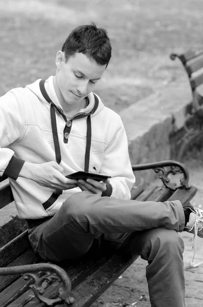 Jeune homme assis sur le banc et utilisant une tablette ou un téléphone intelligent le jour du printemps — Photo