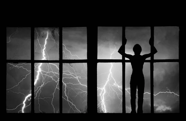 Silhouette of man watching lightning, thunder, rain and storm through broken window of old building — Stock Photo, Image