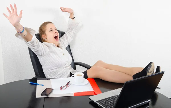 Perezosa mujer de negocios bostezando mientras está sentada en su oficina y bebiendo café — Foto de Stock