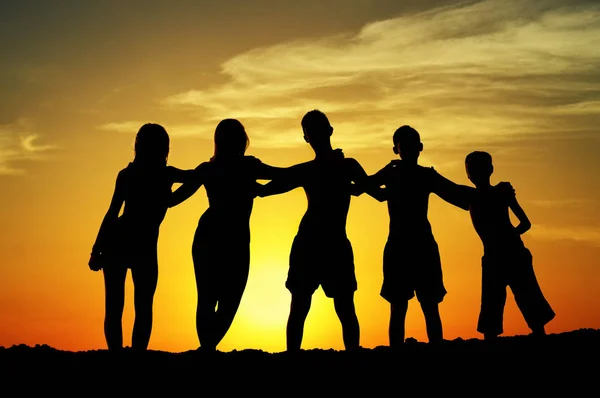 Silhouettes of five teenage boys and girls standing and hugging — Stock Photo, Image