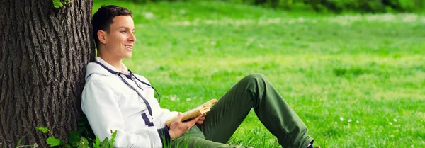 Junger glücklicher Mann liest Buch in der Natur — Stockfoto