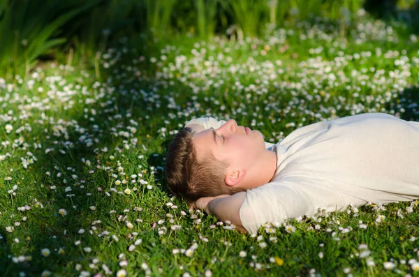 Dospívající chlapec leží na louce plné bílé květy na Sochor — Stock fotografie