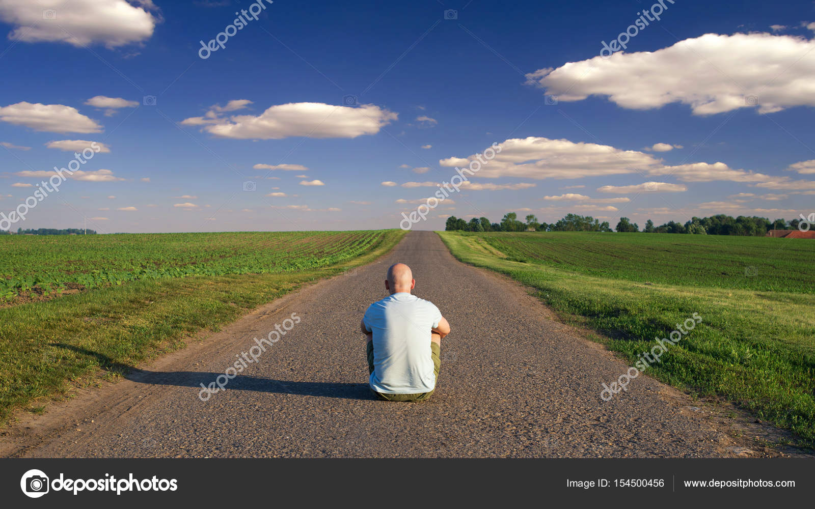 Man sitting in the middle of the country road on sunny summer day