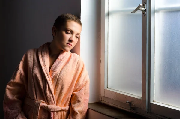 Young woman cancer patient standing in front of the hospital window — Stock Photo, Image
