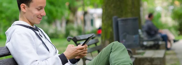 Bankta oturan ve tablet aygıtı kullanarak genç adam Stok Resim