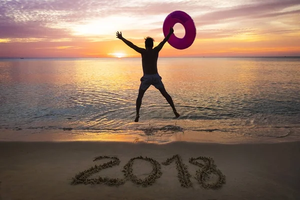 New Year 2018 on beach sand, a man jumping with the floaty during sunset — Stock Photo, Image