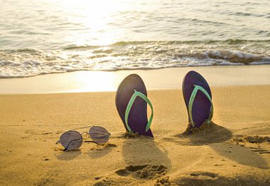 Flip-flop ve gün batımında sahilde güneş gözlüğü