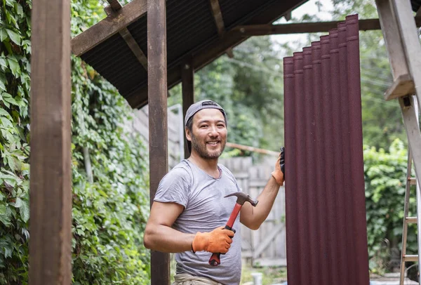 Omul construiește acoperiș și deține ciocan și material de acoperiș . — Fotografie, imagine de stoc