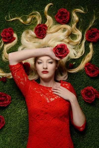 女人躺在草穿件红色的连衣裙，拿着一朵玫瑰 — 图库照片