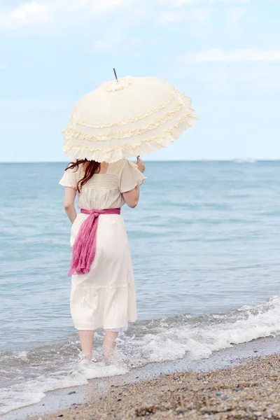 Vintage woman with parasol standing in the water on beach — Stock Photo, Image