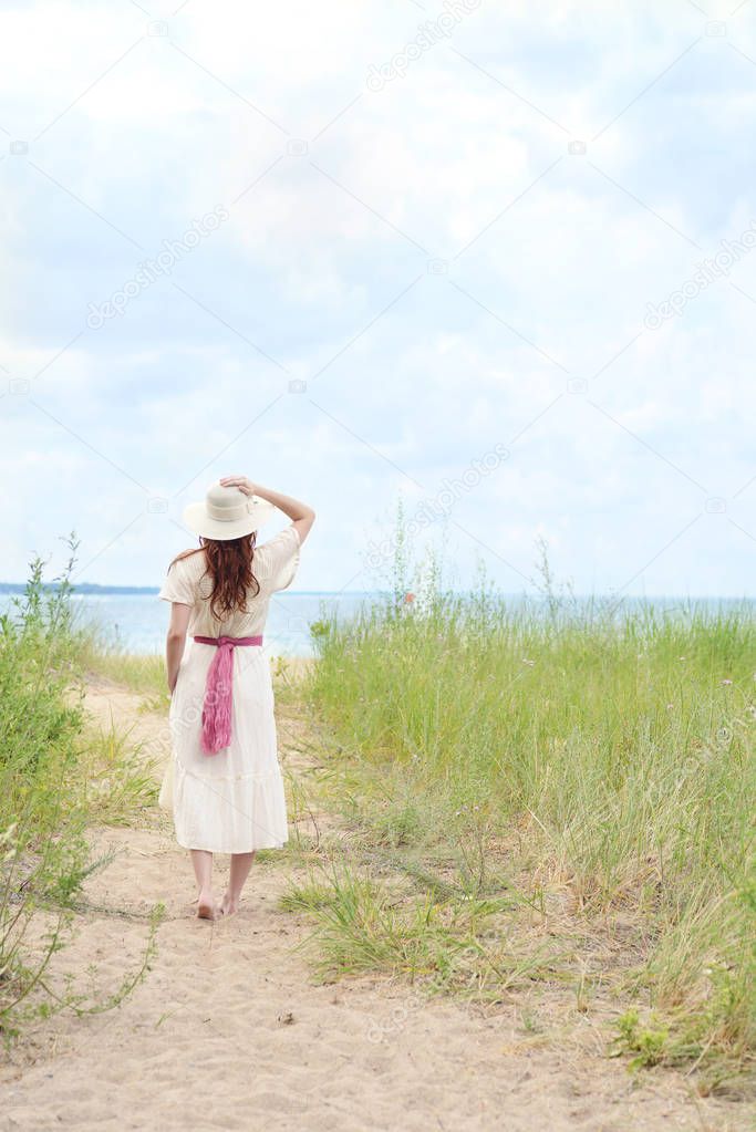vintage redhead woman holding her hat on the beach